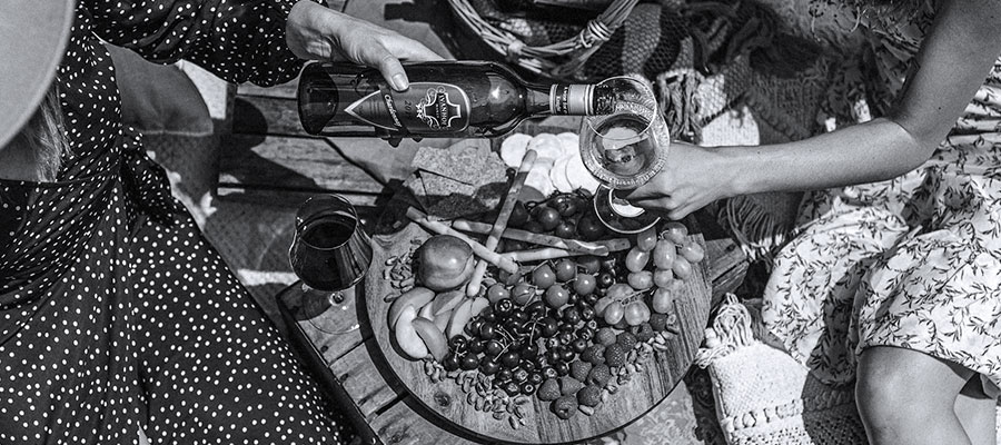 People sharing a bottle of Ivanhoe wine over a picnic of fruit