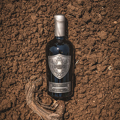 A bottle of Ivanhoe King's Ransom Liqueur Cabernet Sauvignon nestled in the soil next to a vine root