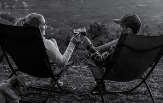 Two people on camping chairs cheersing glasses of wine