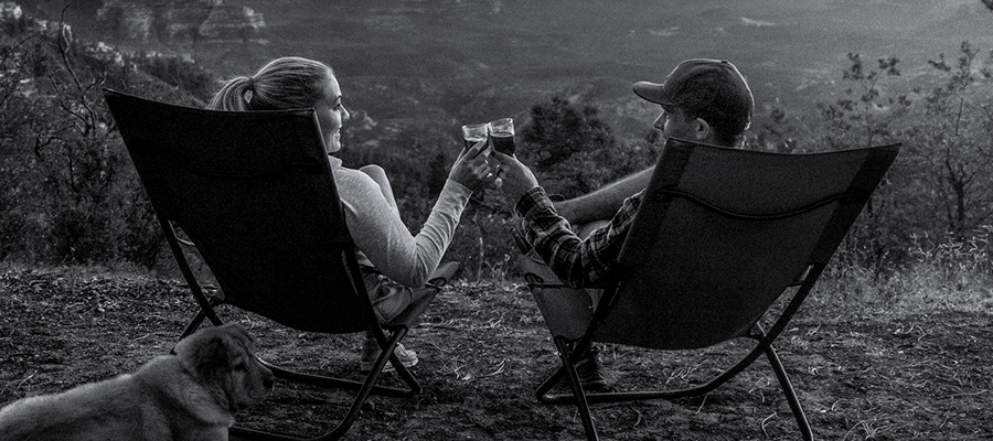 Two people on camping chairs cheersing glasses of wine